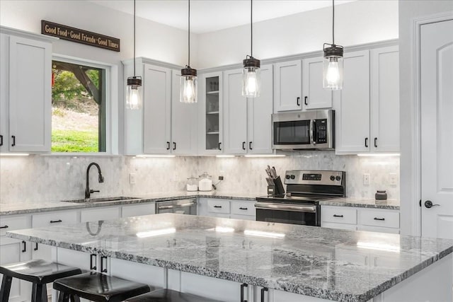 kitchen featuring stainless steel appliances, glass insert cabinets, hanging light fixtures, and a sink