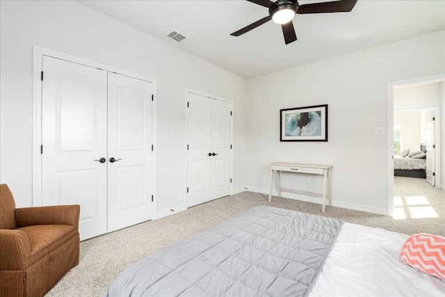 bedroom with baseboards, visible vents, multiple closets, and light colored carpet