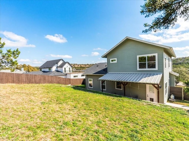 rear view of property featuring a yard, metal roof, and fence