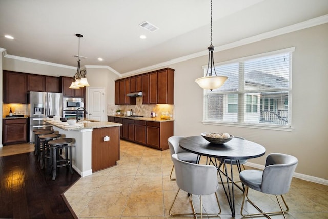 kitchen with pendant lighting, tasteful backsplash, an island with sink, and appliances with stainless steel finishes