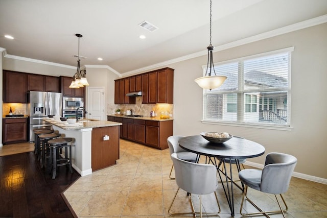 kitchen featuring appliances with stainless steel finishes, an island with sink, tasteful backsplash, under cabinet range hood, and visible vents