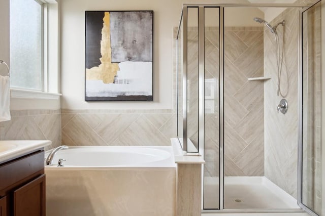 full bath with vanity, a bath, a stall shower, and tile walls