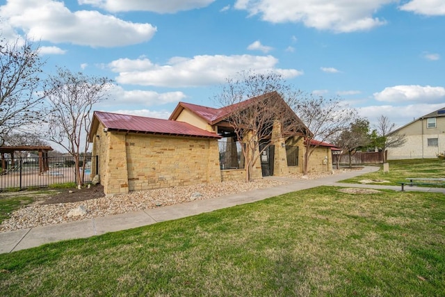 rear view of house featuring fence, a lawn, metal roof, and stone siding