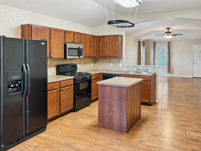 kitchen featuring sink, a center island, light hardwood / wood-style floors, decorative backsplash, and black appliances