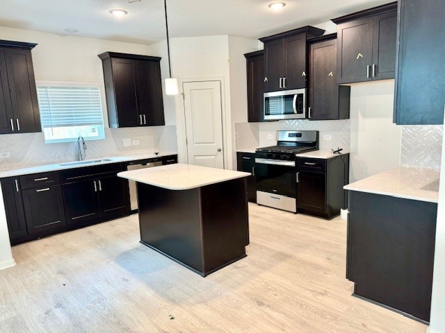 kitchen featuring sink, appliances with stainless steel finishes, a kitchen island, decorative light fixtures, and light wood-type flooring