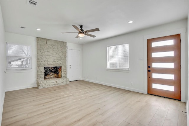 unfurnished living room with visible vents, a stone fireplace, light wood-type flooring, and baseboards