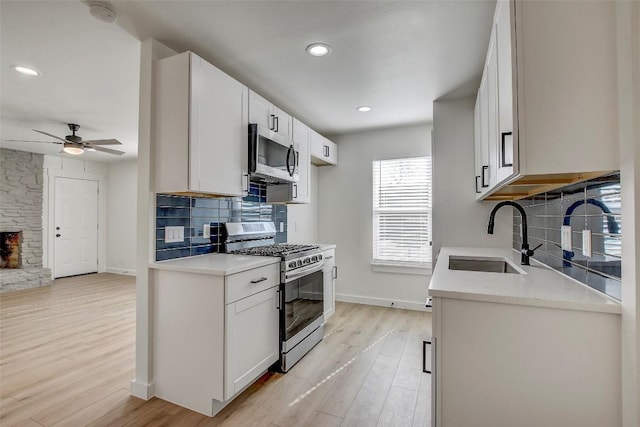 kitchen featuring a ceiling fan, a sink, backsplash, stainless steel appliances, and light wood finished floors