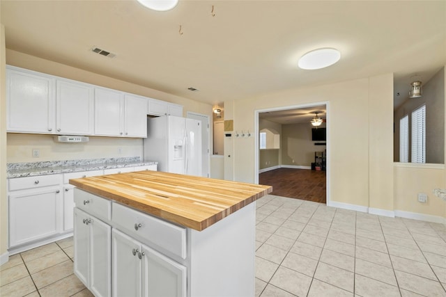 kitchen with white cabinetry, a center island, white refrigerator with ice dispenser, and wood counters