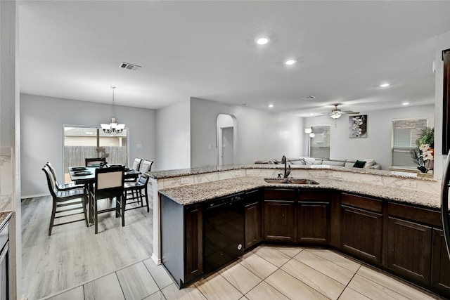 kitchen with dark brown cabinets, a sink, light stone counters, ceiling fan with notable chandelier, and black dishwasher