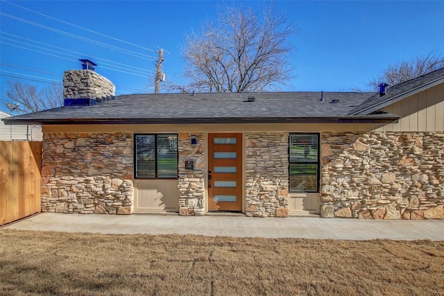 entrance to property with stone siding, fence, a yard, roof with shingles, and a chimney