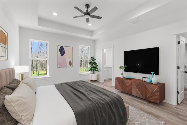 bedroom featuring multiple windows, a tray ceiling, and light hardwood / wood-style flooring