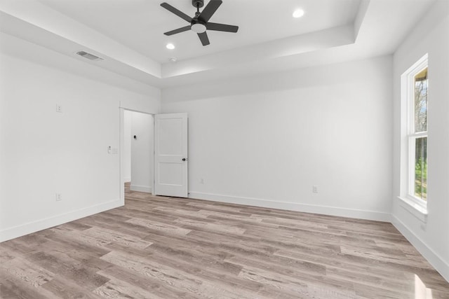 unfurnished room with a tray ceiling, light hardwood / wood-style floors, and a healthy amount of sunlight