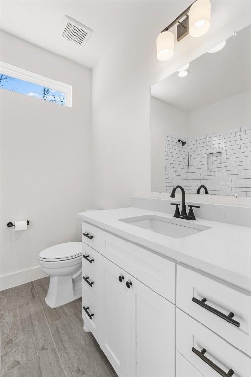 bathroom with vanity, wood-type flooring, tiled shower, and toilet