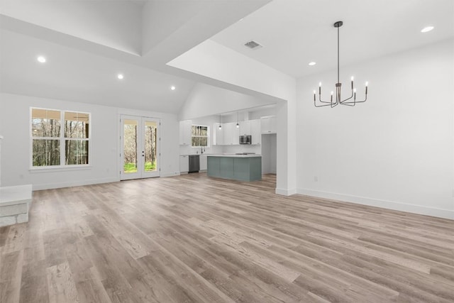 unfurnished living room with high vaulted ceiling, an inviting chandelier, light hardwood / wood-style floors, and french doors