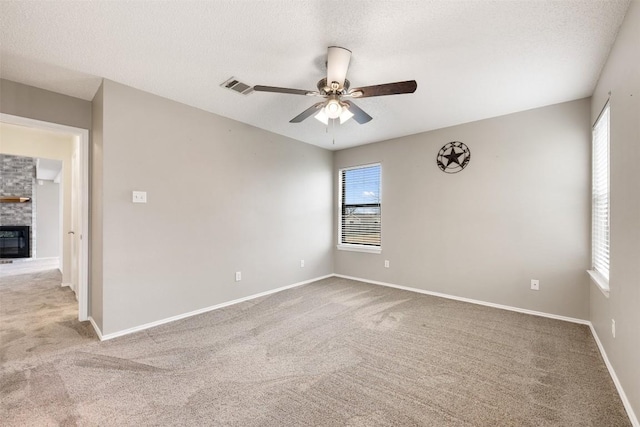 carpeted empty room with ceiling fan, a large fireplace, a wealth of natural light, and a textured ceiling