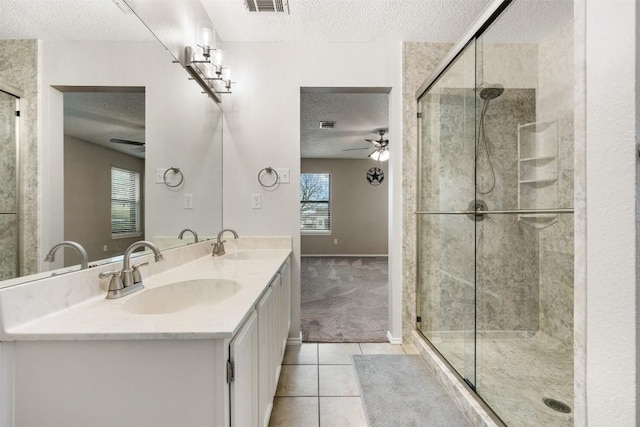 bathroom with ceiling fan, vanity, a textured ceiling, a shower with shower door, and tile patterned floors