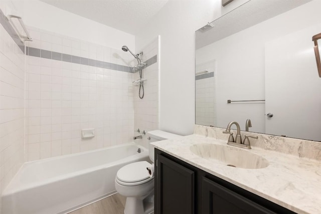 full bathroom featuring hardwood / wood-style flooring, tiled shower / bath combo, vanity, a textured ceiling, and toilet