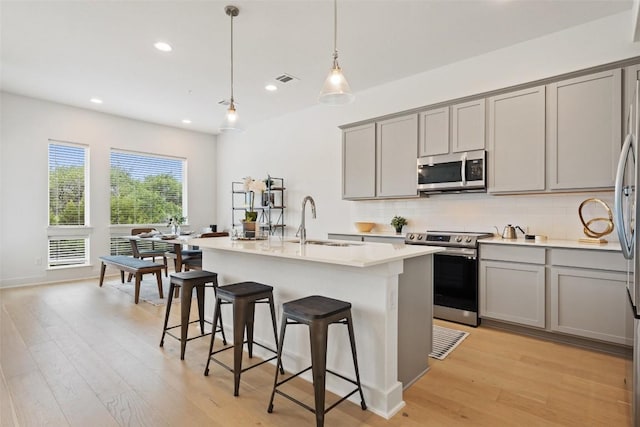 kitchen featuring sink, a center island with sink, appliances with stainless steel finishes, pendant lighting, and decorative backsplash