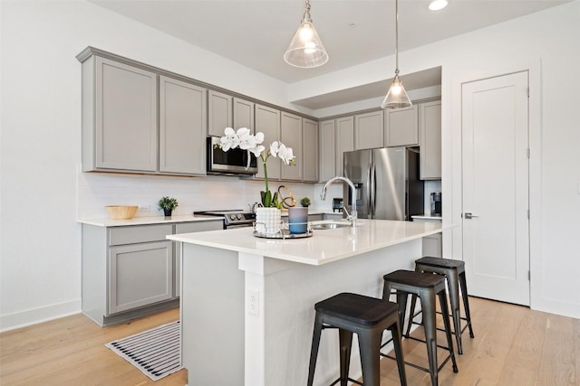 kitchen featuring a kitchen bar, a center island with sink, light wood-type flooring, gray cabinets, and stainless steel appliances