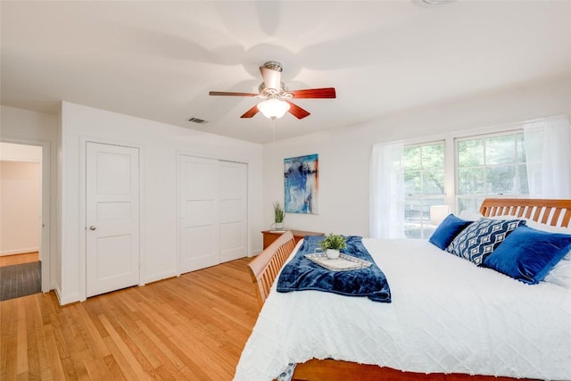 bedroom with hardwood / wood-style flooring, ceiling fan, and two closets