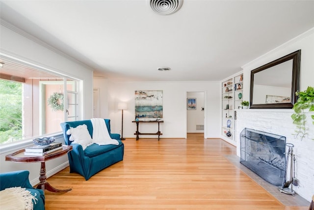 sitting room with a brick fireplace, hardwood / wood-style flooring, ornamental molding, and built in shelves