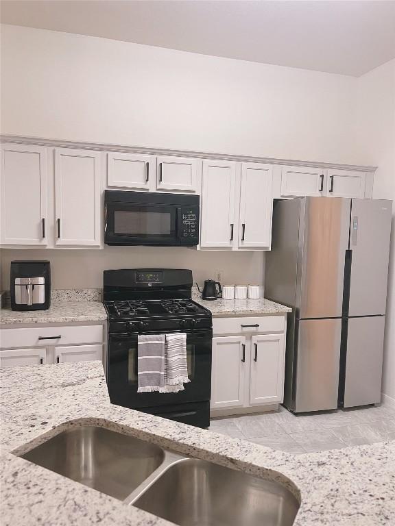 kitchen with sink, black appliances, white cabinets, and light stone countertops