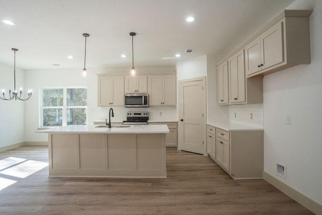 kitchen with sink, hanging light fixtures, stainless steel appliances, and an island with sink