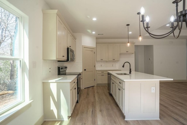 kitchen with decorative light fixtures, white cabinetry, sink, stainless steel appliances, and a center island with sink