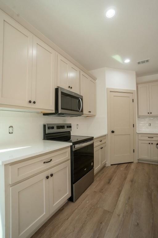 kitchen with stainless steel appliances, backsplash, and light hardwood / wood-style flooring