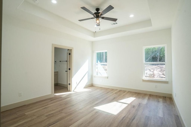 empty room with a raised ceiling, a wealth of natural light, and light wood-type flooring