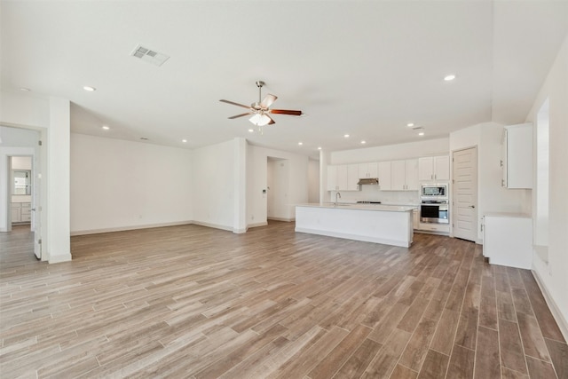 unfurnished living room with ceiling fan, sink, and light wood-type flooring