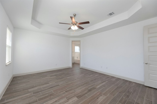 empty room featuring ceiling fan, wood-type flooring, and a tray ceiling