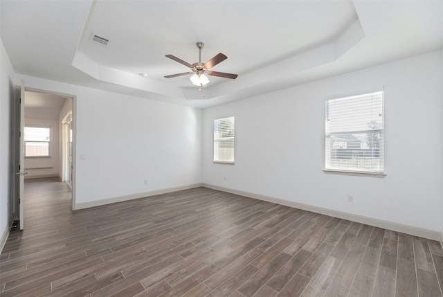 unfurnished room with a raised ceiling, dark hardwood / wood-style floors, and ceiling fan