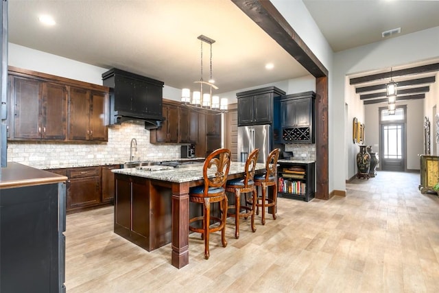 kitchen featuring dark brown cabinets, decorative light fixtures, stainless steel fridge with ice dispenser, and a center island with sink