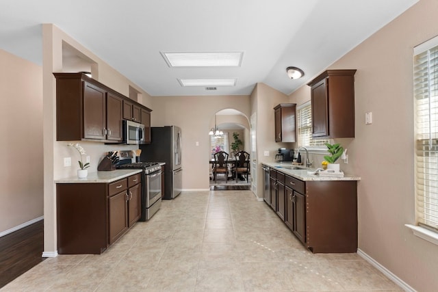 kitchen with light tile patterned flooring, appliances with stainless steel finishes, sink, dark brown cabinetry, and light stone countertops