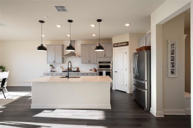 kitchen featuring gray cabinets, an island with sink, appliances with stainless steel finishes, and pendant lighting