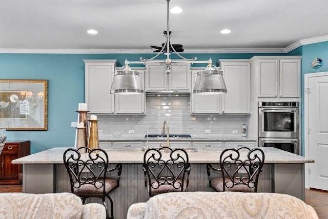 kitchen featuring decorative light fixtures, light stone countertops, a kitchen island with sink, and a breakfast bar area