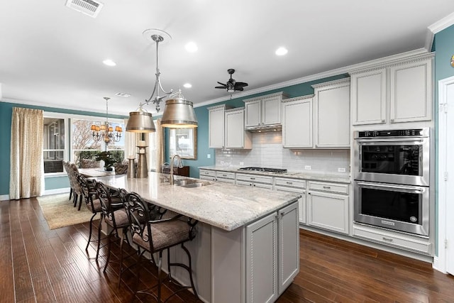 kitchen with sink, light stone counters, decorative light fixtures, a center island with sink, and stainless steel appliances