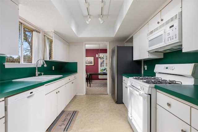 kitchen with sink, white cabinetry, a chandelier, a tray ceiling, and white appliances