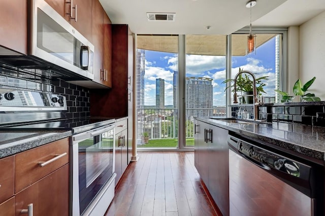 kitchen featuring appliances with stainless steel finishes, tasteful backsplash, expansive windows, a view of city, and dark wood-type flooring
