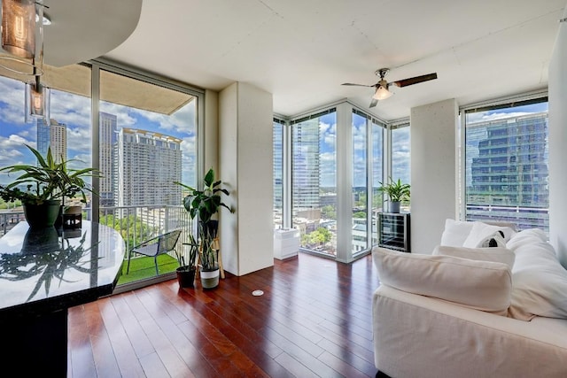 living area with a view of city, a ceiling fan, expansive windows, and hardwood / wood-style flooring