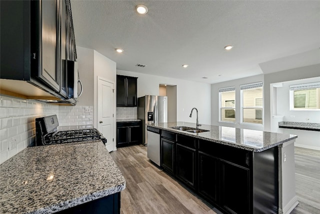 kitchen with a kitchen island with sink, sink, light stone counters, and stainless steel appliances