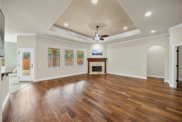 unfurnished living room with ceiling fan, dark hardwood / wood-style floors, a fireplace, ornamental molding, and a raised ceiling