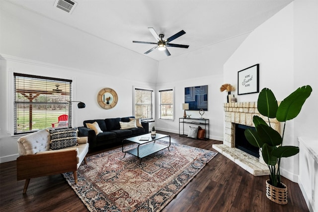 living room with a stone fireplace, dark wood-type flooring, ceiling fan, and vaulted ceiling