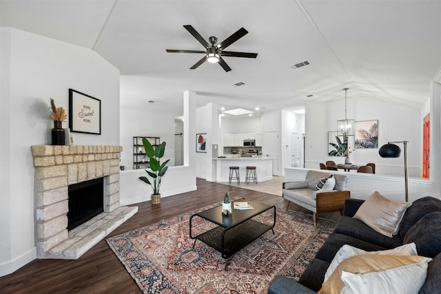 living room featuring ceiling fan with notable chandelier, a fireplace, vaulted ceiling, and hardwood / wood-style floors