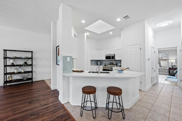 kitchen featuring sink, appliances with stainless steel finishes, a skylight, white cabinets, and kitchen peninsula