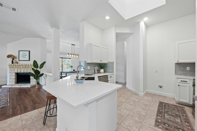 kitchen featuring lofted ceiling with skylight, a fireplace, white cabinetry, sink, and hanging light fixtures