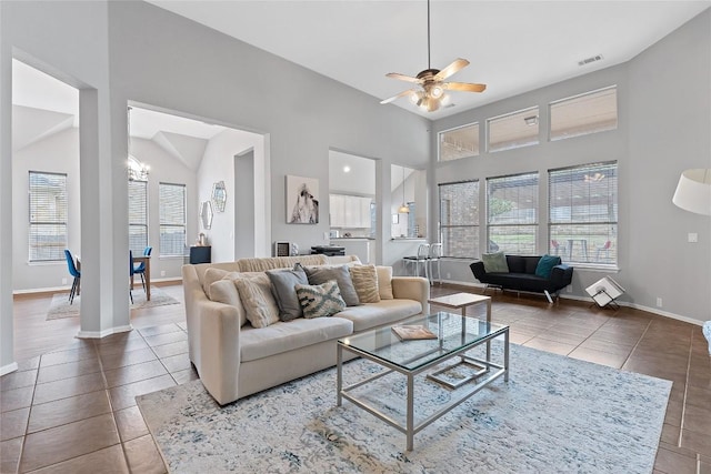 tiled living room with ceiling fan with notable chandelier and high vaulted ceiling