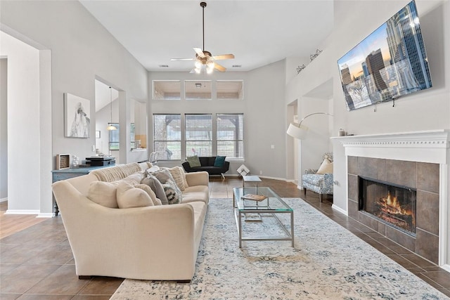 living room featuring dark tile patterned floors, a fireplace, ceiling fan, and a high ceiling