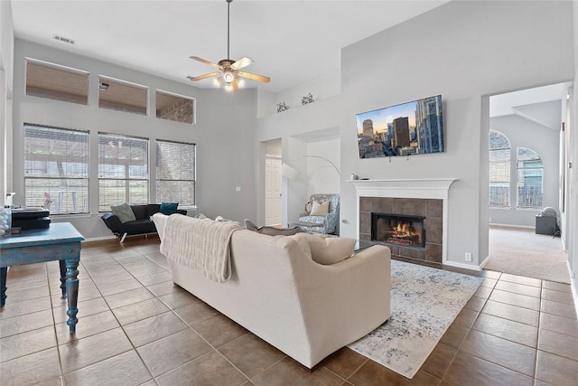 tiled living room featuring a tiled fireplace, a towering ceiling, and ceiling fan